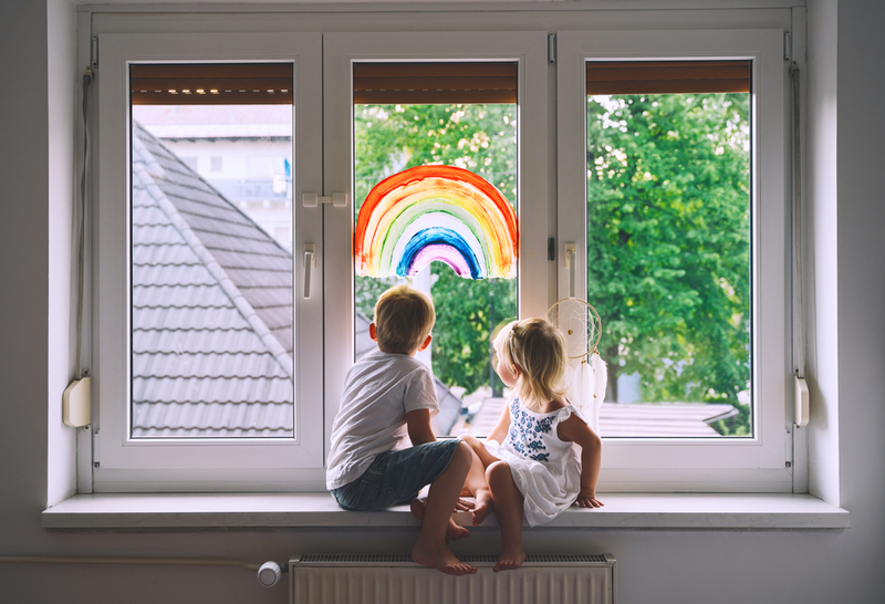 Kids sitting in front of a window with a rainbow painted on it.
