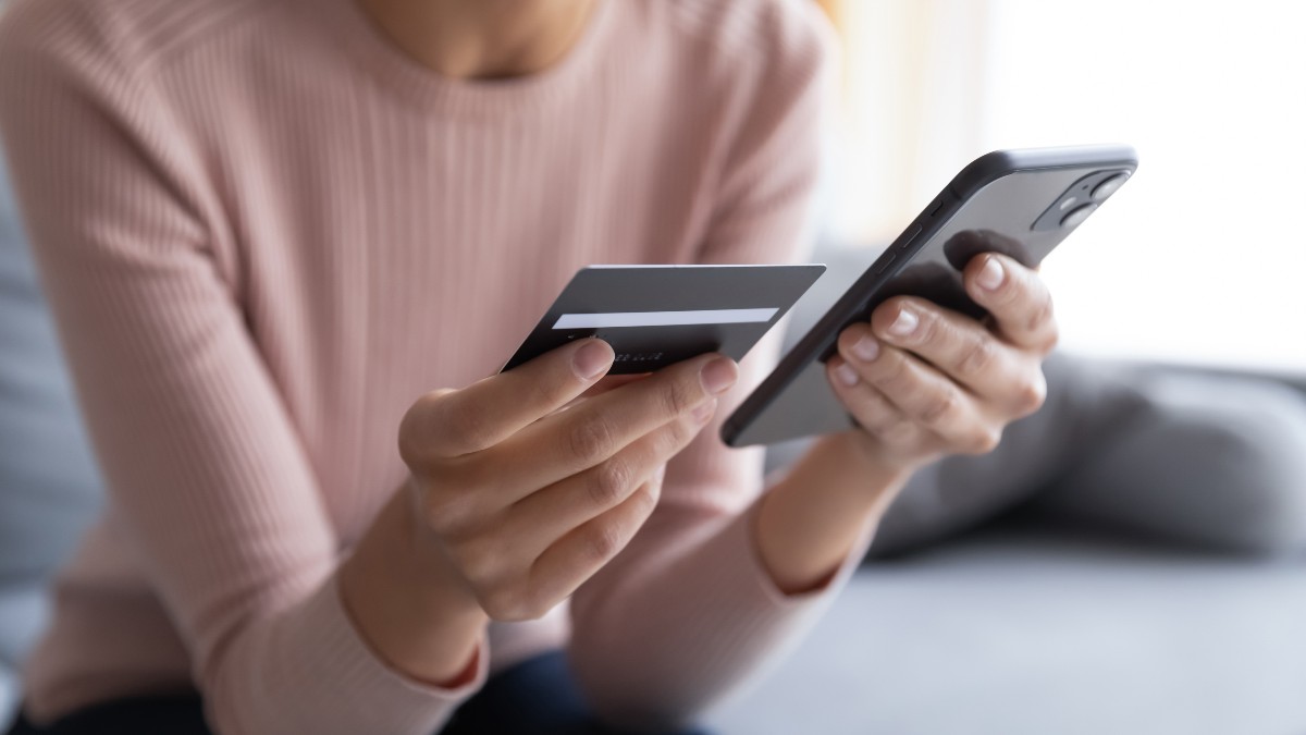 Individual holding credit card and cellphone.