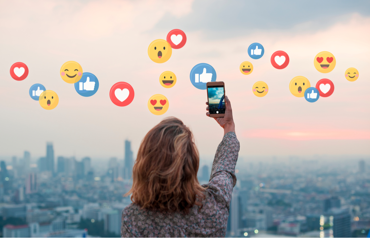 Woman taking picture of skyline with emojis in the air.