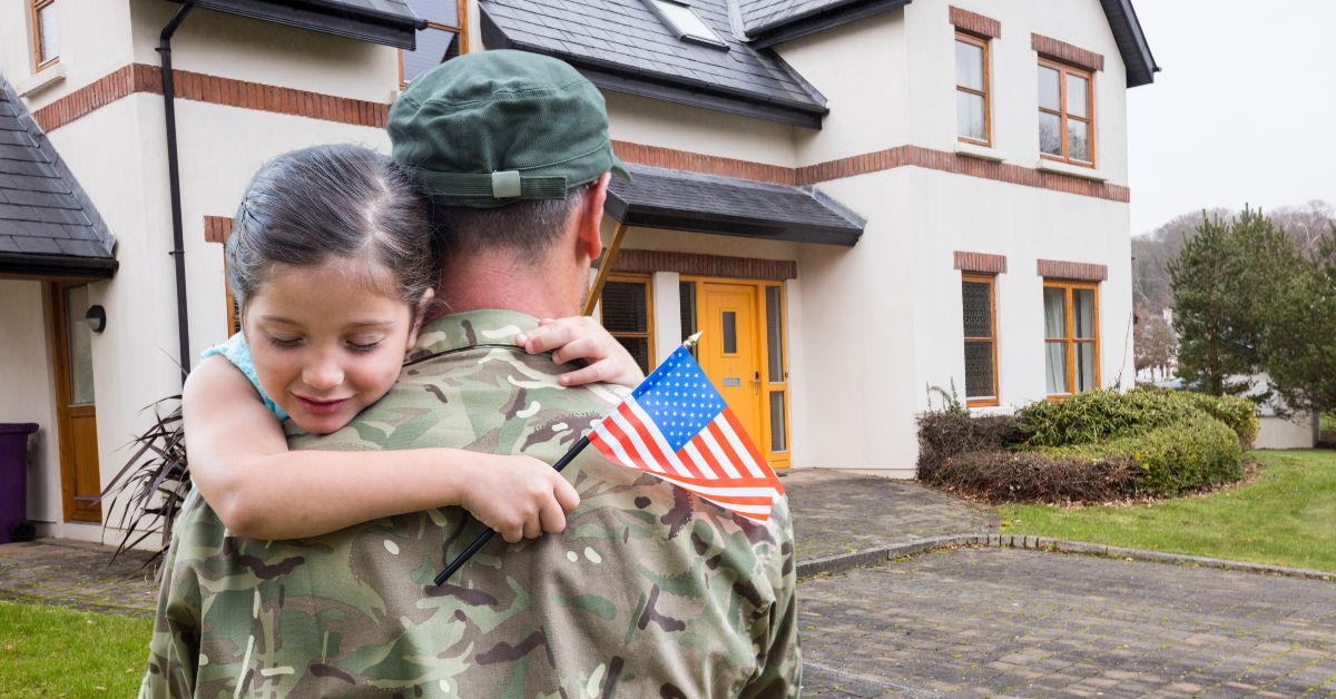 Military member hugging child in front of home.